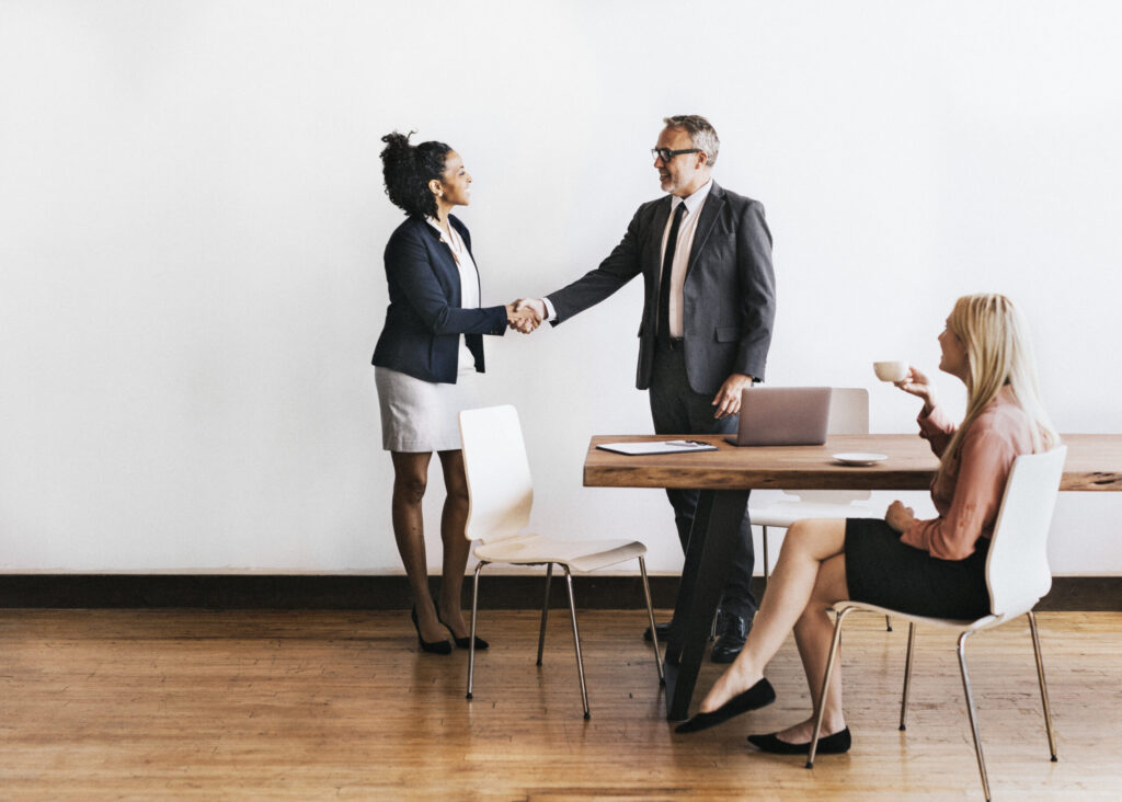 A sales professional arriving at her clients’ office and shaking hands with one of them.